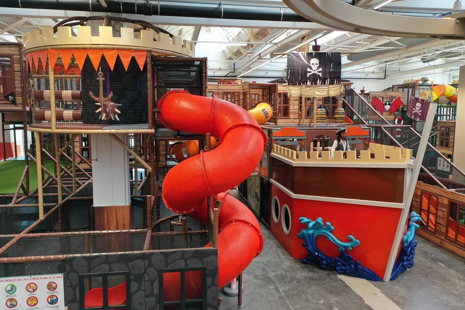 Structure de jeux indoor géante sur le thème des pirates avec bateau et grand toboggan spiralé, conçue sur mesure par Play In Business pour le parc L'Île de Tortuga à Lille.